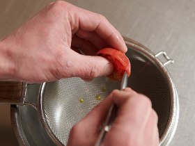 ・種を取る作業時にしたたるトマトの果汁もソースに使うので、網ザルとボウルを重ねた上で作業する。<br>・皮と種と取り除くことで、舌触りがなめらかなトマトソースになる。